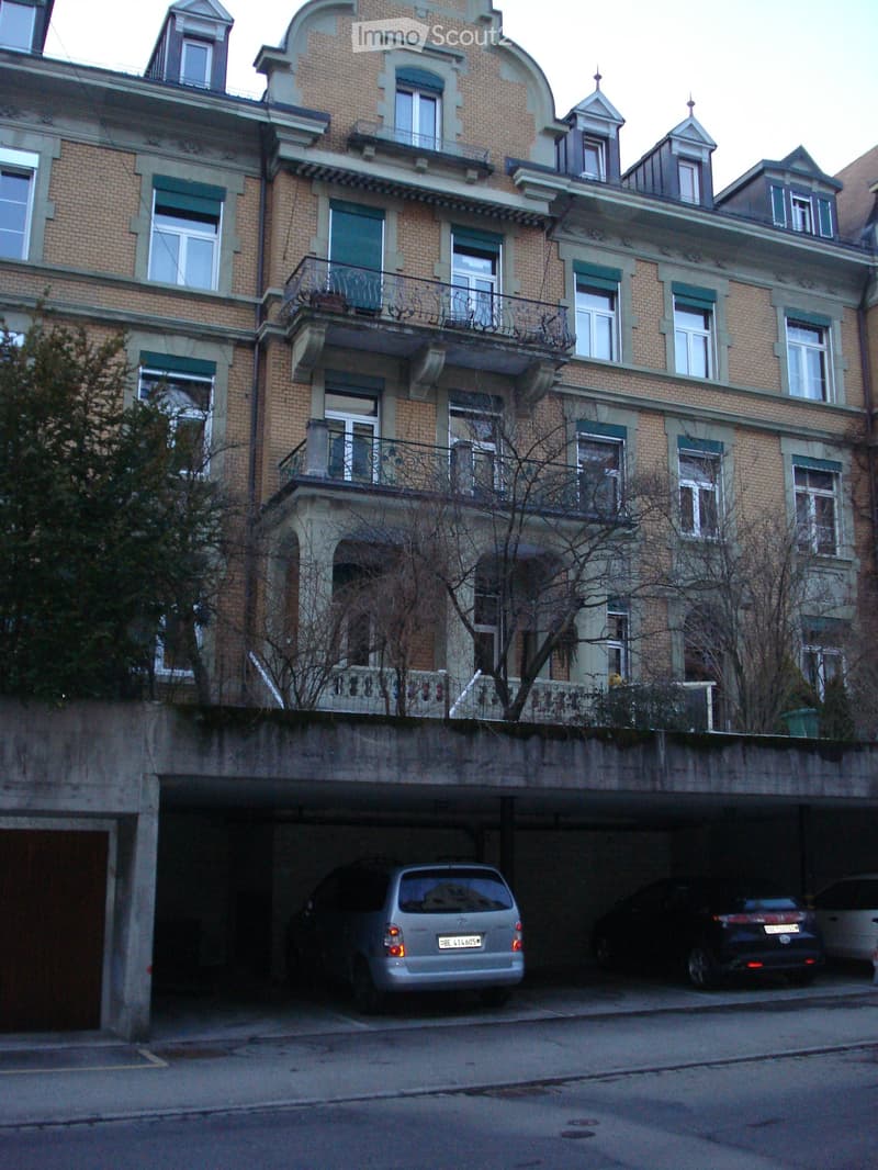 Multi-story brick building with balconies, ornate architectural details, and a covered parking area below.