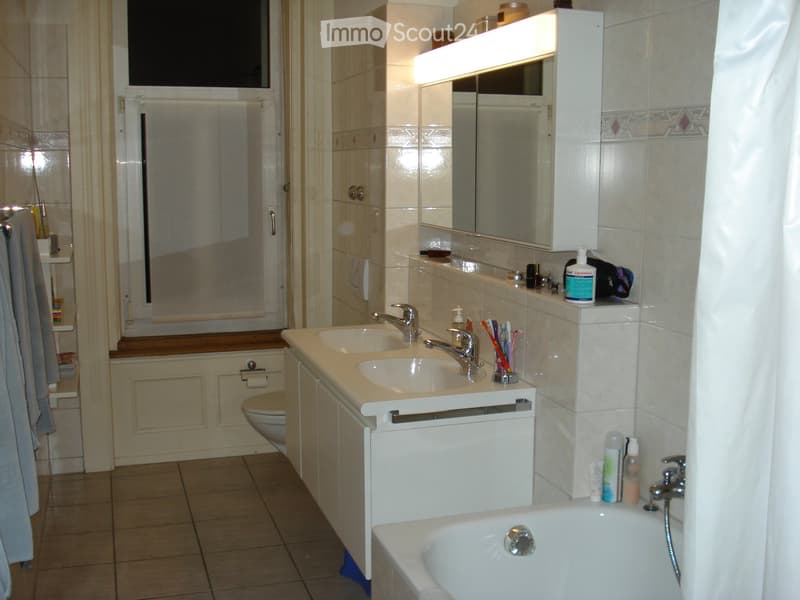 Bathroom with double sink, mirror, bathtub, toilet, and tiled walls.