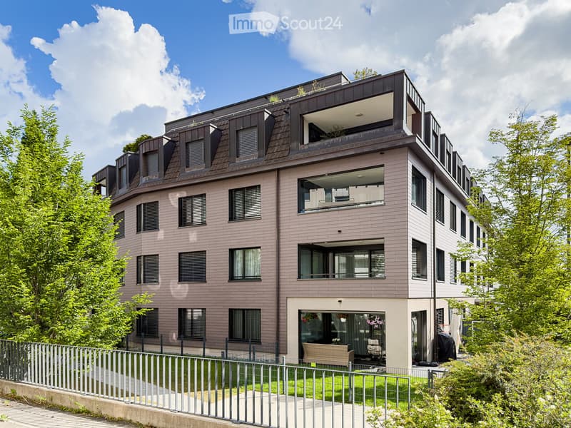 Modern multi-story residential building with a combination of light pink and dark brown facades, large windows, balconies, and a rooftop terrace.