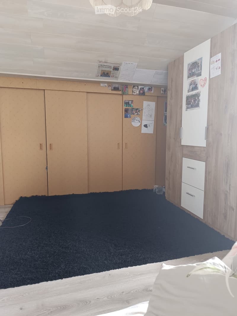 A small, unfurnished room with wooden walls, a black shag rug, a white cabinet, and a refrigerator with picture frames attached to it.
