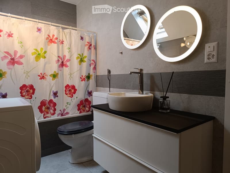 Modern bathroom with a white sink, chrome faucet, round LED mirrors, a toilet, and a floral shower curtain.