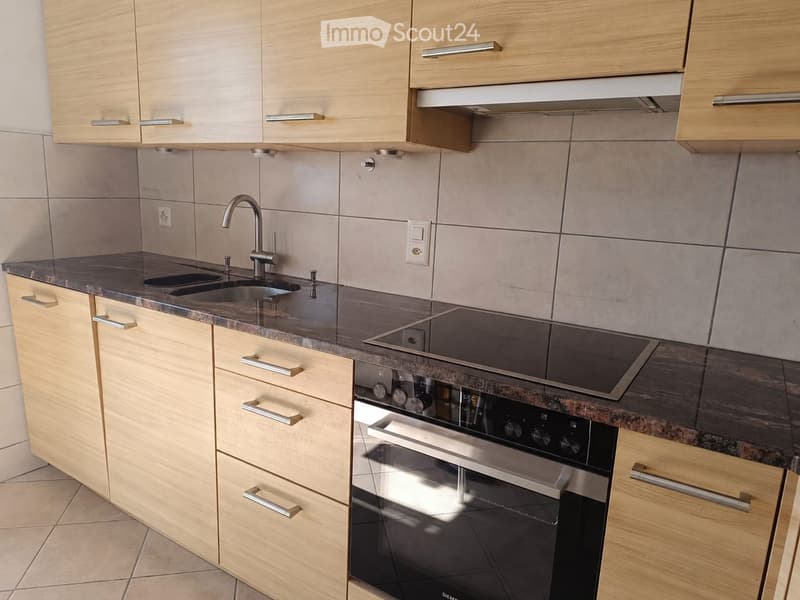Modern kitchen with light wooden cabinets, granite countertops, stainless steel sink, faucet, oven, and induction cooktop.