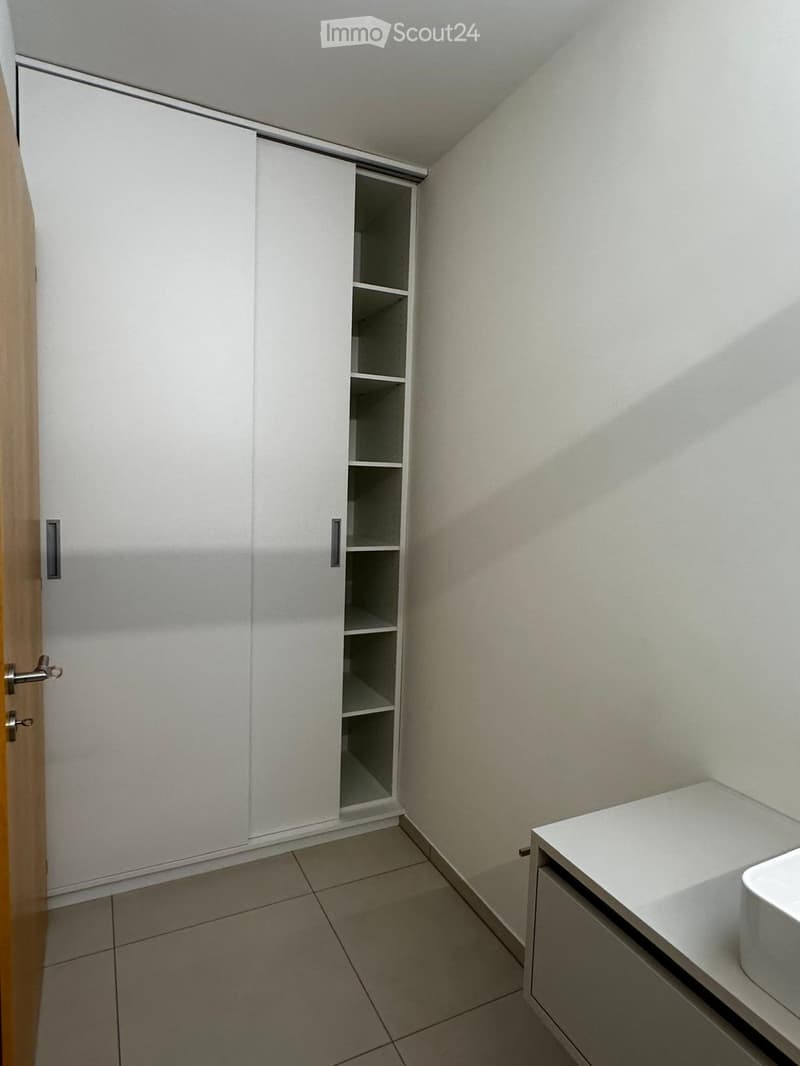 Modern bathroom with white tiled floor, white cabinet, sink, and toilet.