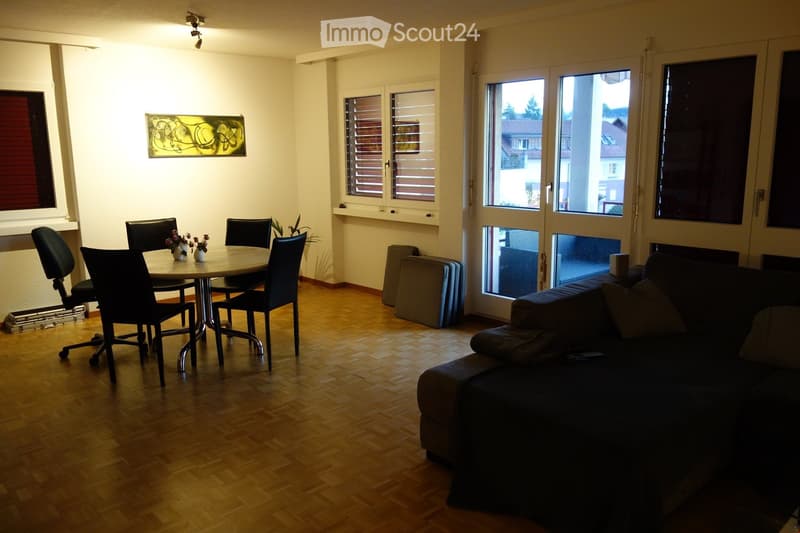 A modern living and dining area with a sofa, dining table, chairs, and decorative vases. The room features large windows and a view of the outside.