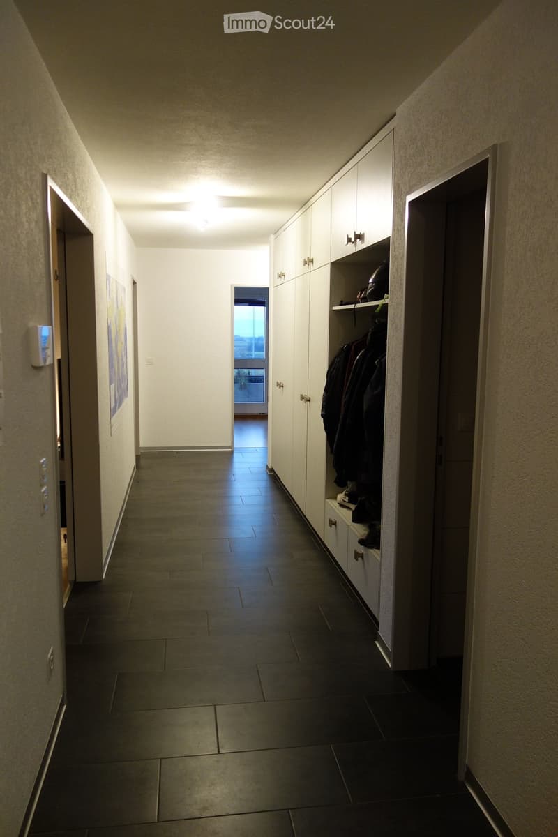 Empty hallway with tiled floor, white walls, built-in storage unit with coats and shoes, and a window at the end.