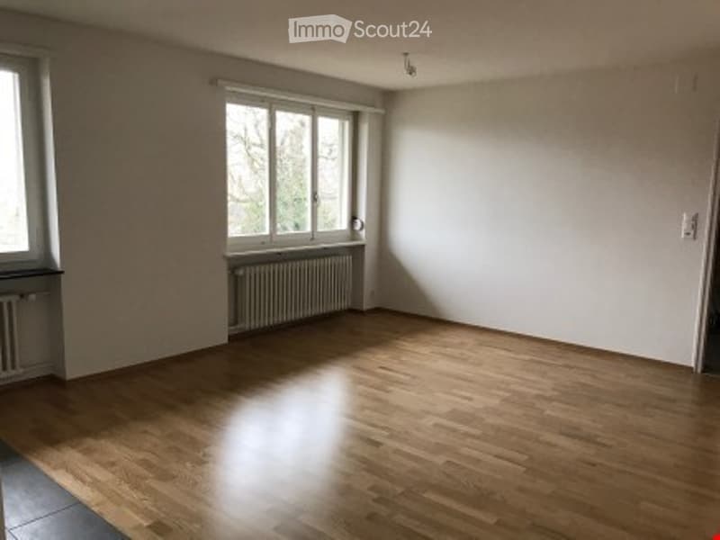 Empty room with wooden flooring, white walls, and large windows allowing natural light. No furniture or equipment present.