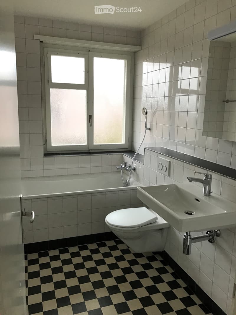 Bathroom with white tiled walls, black and white checkered floor, toilet, sink, bathtub, and showerhead.