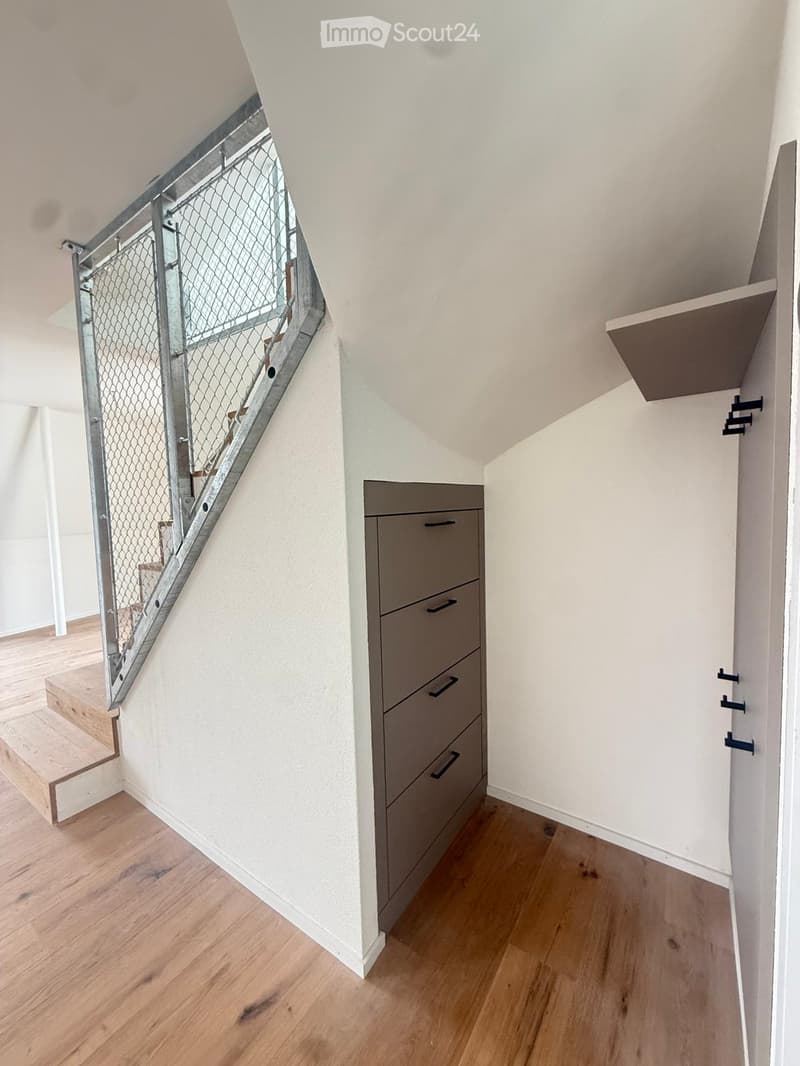 Modern hallway with wooden flooring, white walls, built-in storage unit with drawers, and a staircase with a metal railing leading upwards.