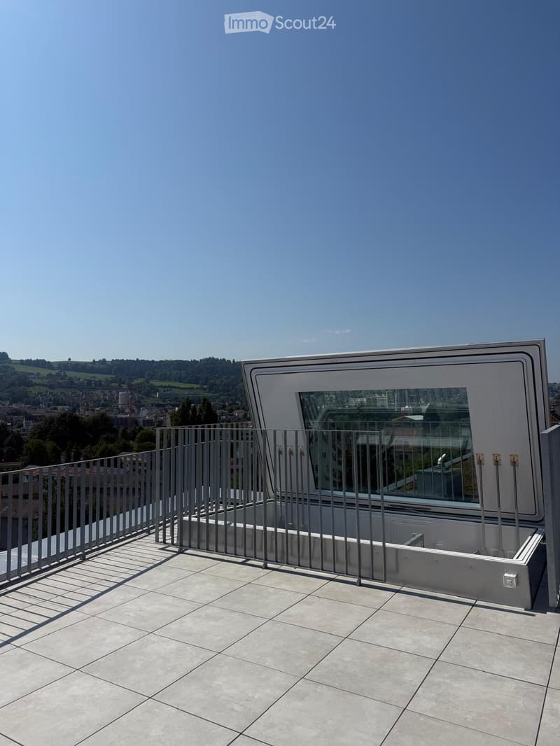 Modern rooftop terrace with tiled flooring, metal railing, and a retractable roof system, offering panoramic city and landscape views.