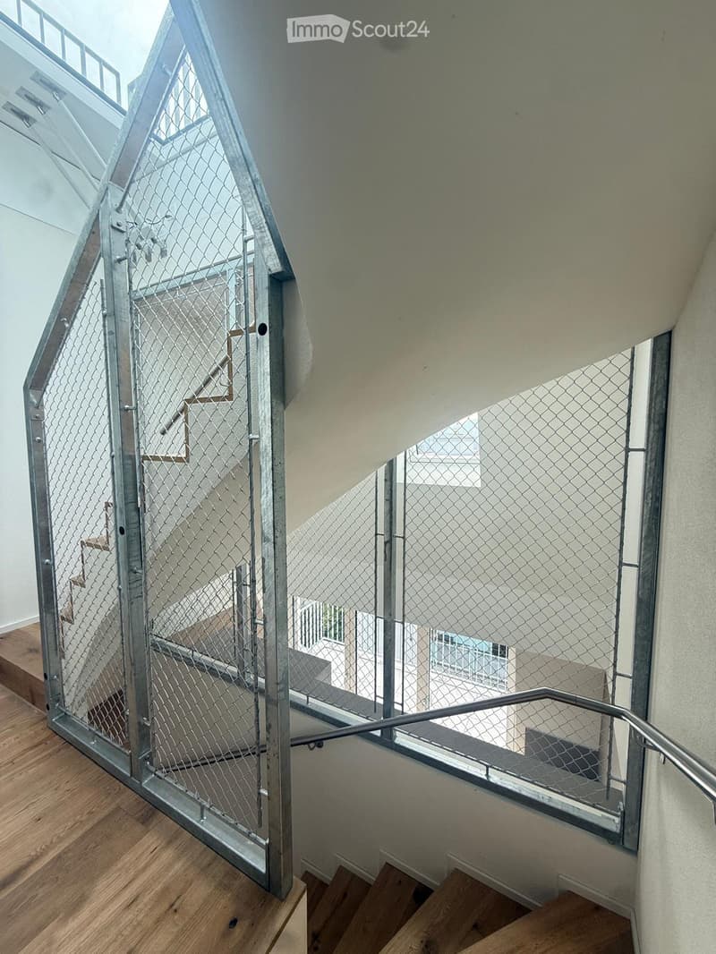 Modern interior staircase with metal railing and wooden steps, featuring a contemporary design with a glass-like balustrade and open structure.