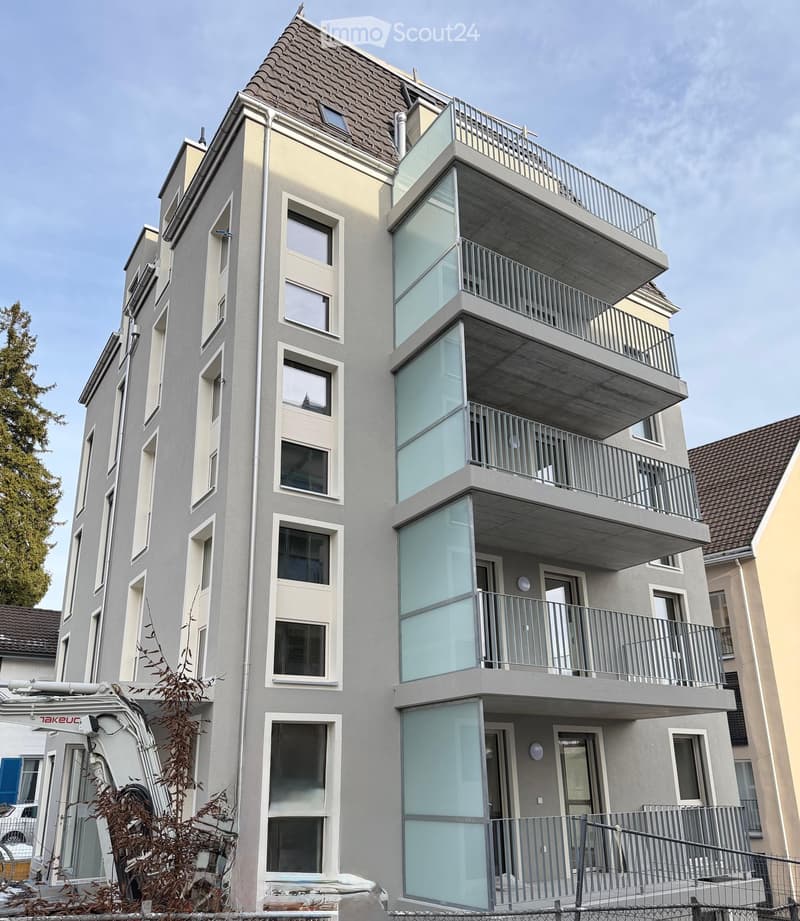 Modern multi-story residential building with grey facade, large windows, and multiple balconies with metal railings.