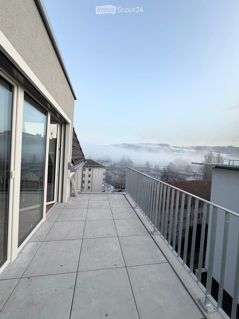 Balcony with concrete tiles, metal railing, and a view of a misty landscape and buildings.