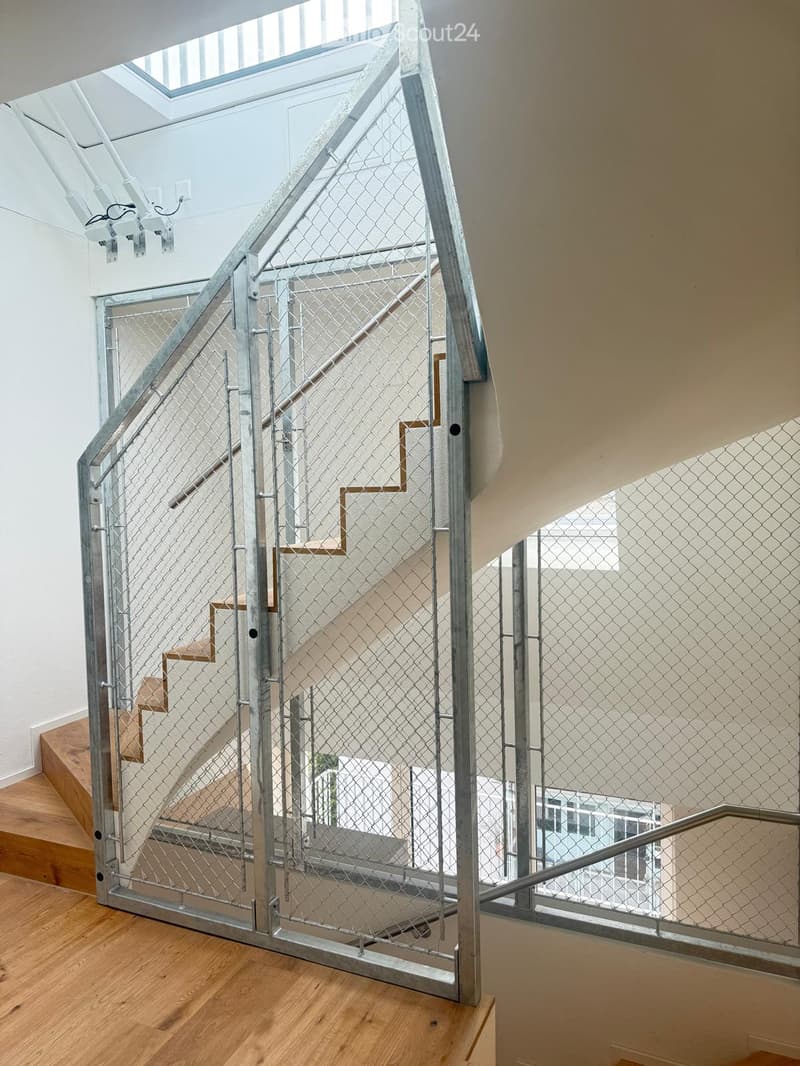 Modern interior staircase with metal railing and wooden steps, featuring a skylight above and white walls.