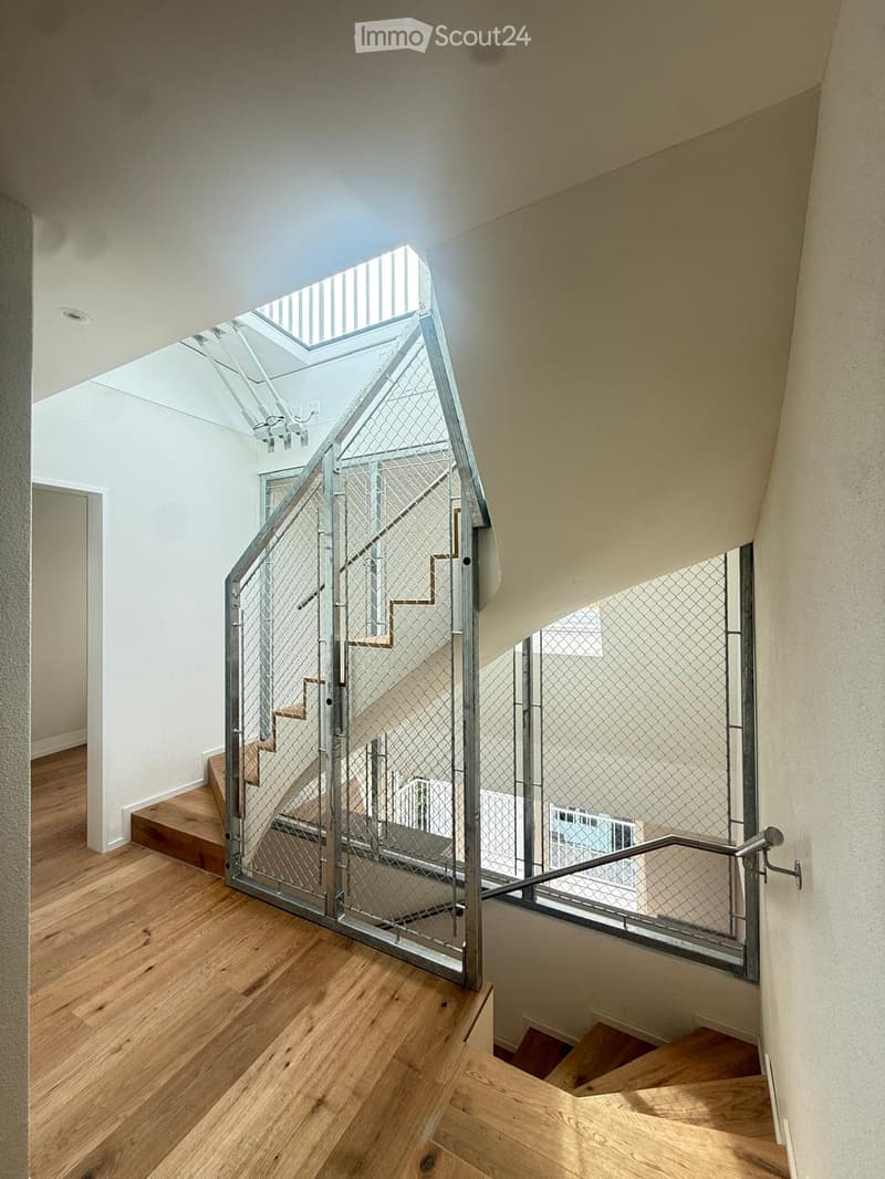 Modern interior staircase with wooden steps, metal railing, and a glass ceiling allowing natural light to filter in.