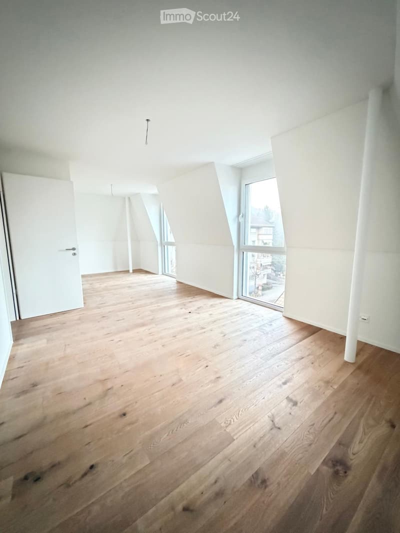 Empty room with wooden flooring, white walls, and large windows offering a view of the outside. No furniture or equipment is present.