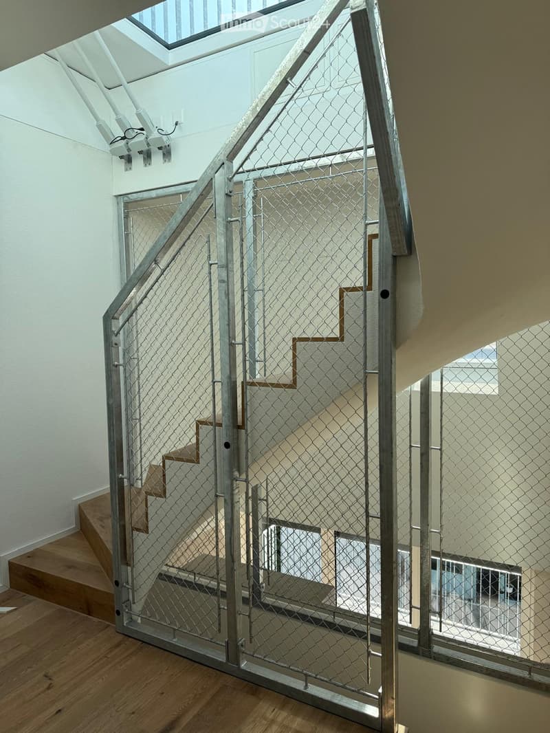 Modern interior staircase with metal railing and wooden steps, leading to an upper level with visible rooms and a skylight above.