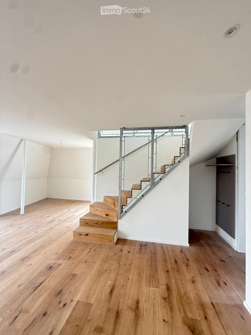Empty room with wooden flooring, white walls, and a staircase leading upwards with a metal railing.