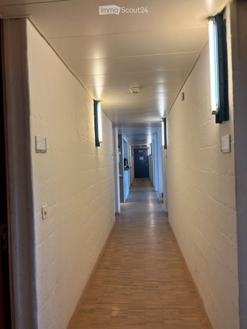 Clean, well-lit hallway with wooden flooring and white walls, featuring integrated lighting and a door at the end.