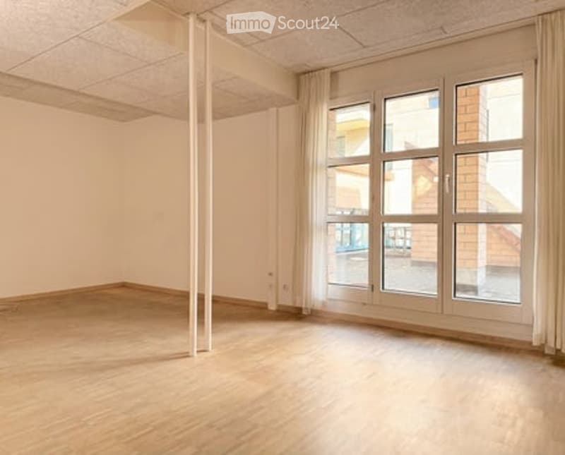Empty room with wooden flooring, white walls, and large windows with curtains. No furniture or equipment present.