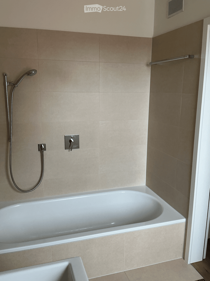 Modern bathroom with a white bathtub, beige tiled walls, and a handheld showerhead mounted on the wall.