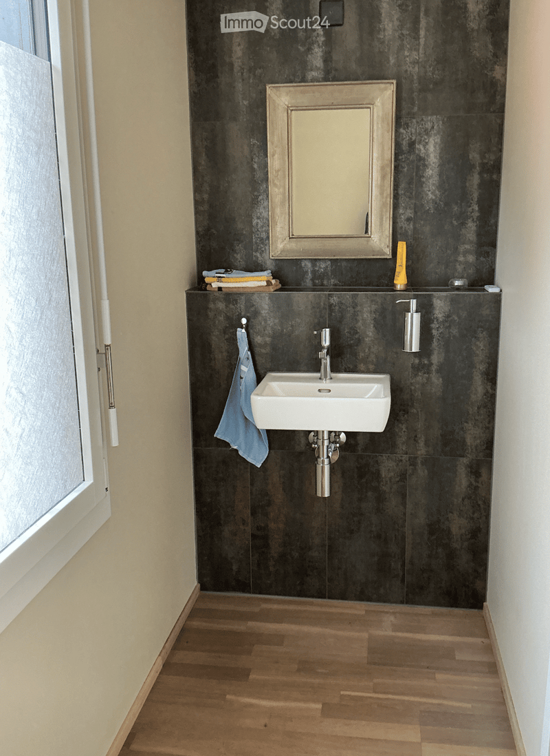 Modern bathroom with dark grey tiled walls, a white sink, a mirror, a towel, and a soap dispenser.