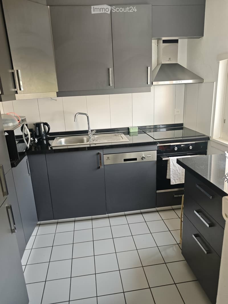 Modern kitchen with grey cabinets, white tiled floor, stainless steel appliances, and a central island.