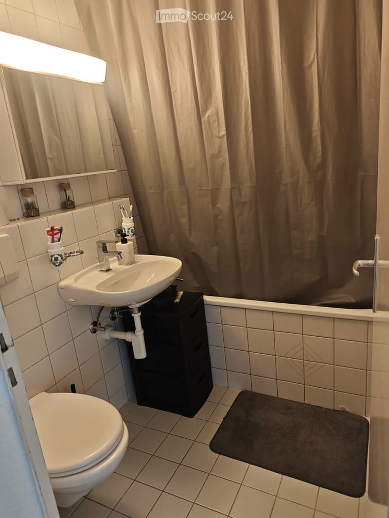 Modern bathroom with white tiles, a toilet, a sink with a mirror, a bathtub with a shower curtain, and a black storage cabinet under the sink.