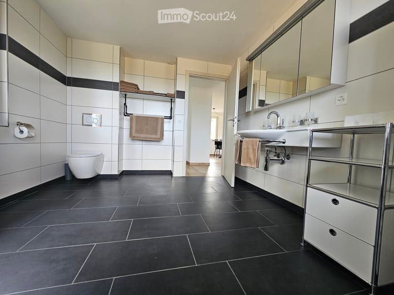 Modern bathroom with black tiled floor, white tiled walls, a toilet, a sink with a mirror, and a towel rack with towels.