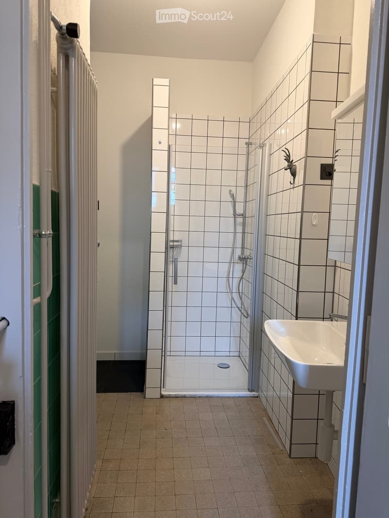 Modern bathroom with white tiled walls, a glass-enclosed shower, a white sink, and a tiled floor.