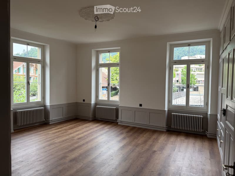 Empty room with wooden flooring, large windows, radiators, and a decorative ceiling light fixture.