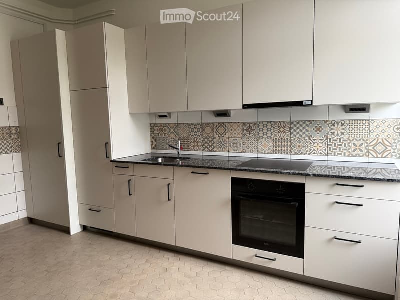 Modern kitchen with white cabinets, granite countertop, sink, faucet, and built-in oven. Decorative tile backsplash with geometric patterns.