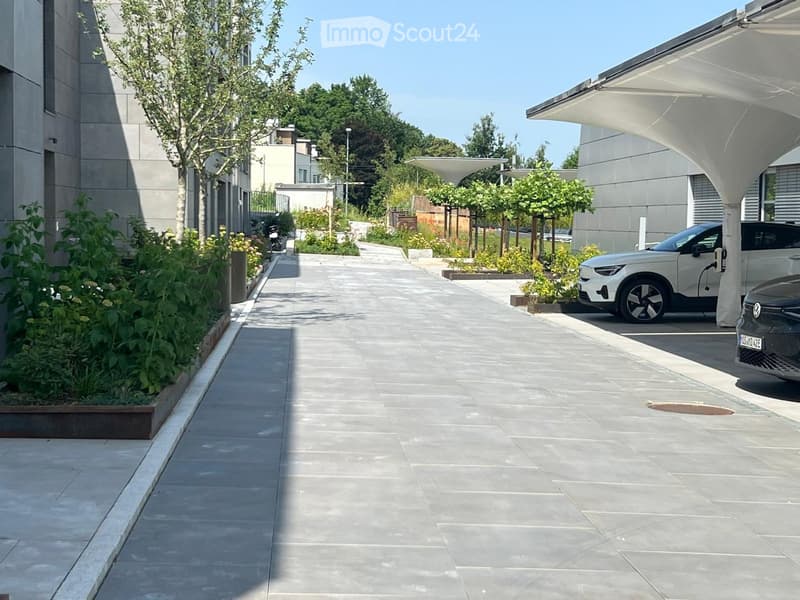 Modern outdoor area with paved walkways, landscaped greenery, and a covered parking area for vehicles.