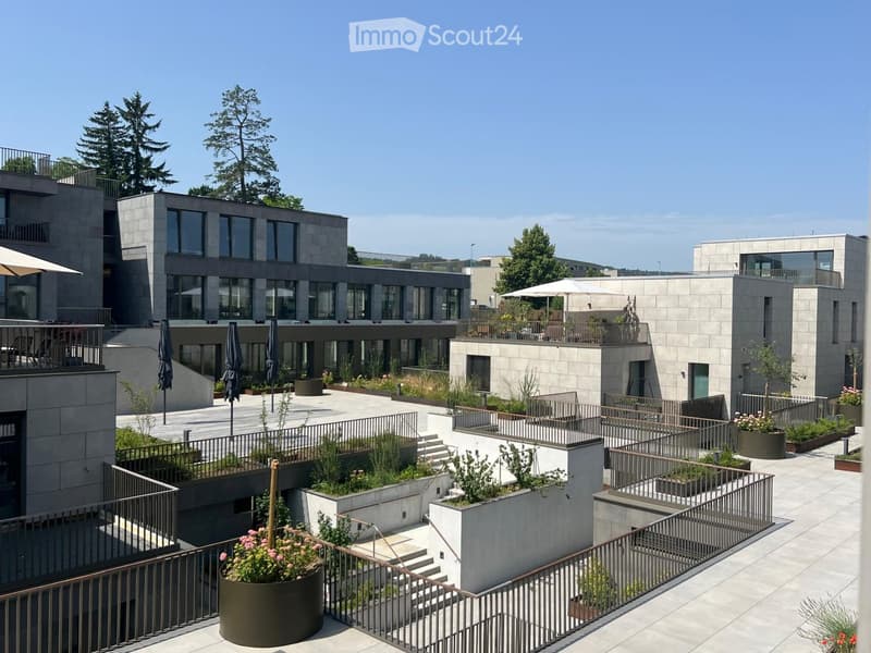 Modern rooftop garden with raised planters, seating areas, and umbrellas, surrounded by contemporary buildings.