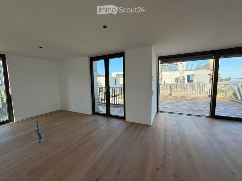 Empty room with wooden flooring, large windows, and sliding glass doors leading to a balcony.