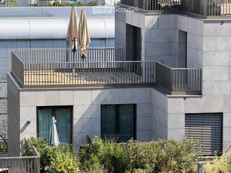 Modern building with grey facade, large windows, and balconies featuring metal railings and closed umbrellas.