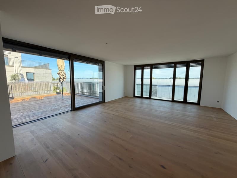 Empty room with wooden flooring, large sliding glass doors leading to a balcony, and bright natural light.