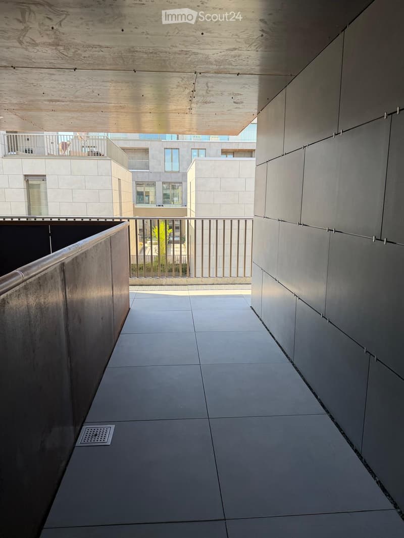 Modern covered corridor with tiled floor, metal railing, and a view of adjacent buildings and balconies.