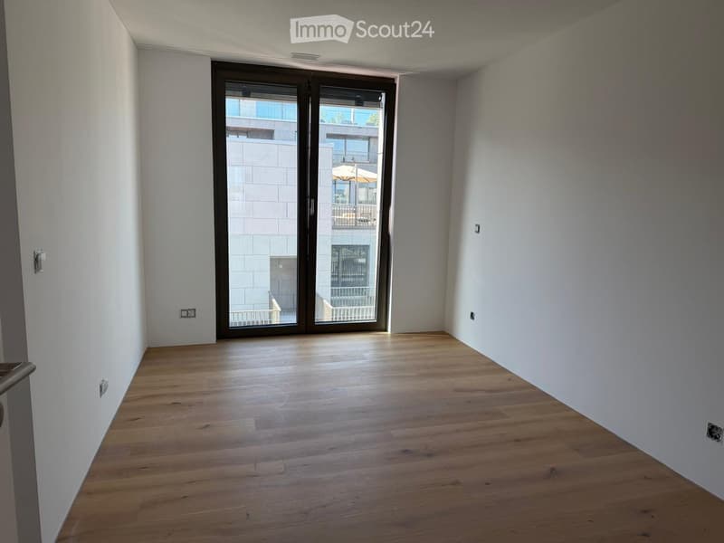 Empty room with wooden flooring, white walls, and a large sliding glass door leading to a balcony.