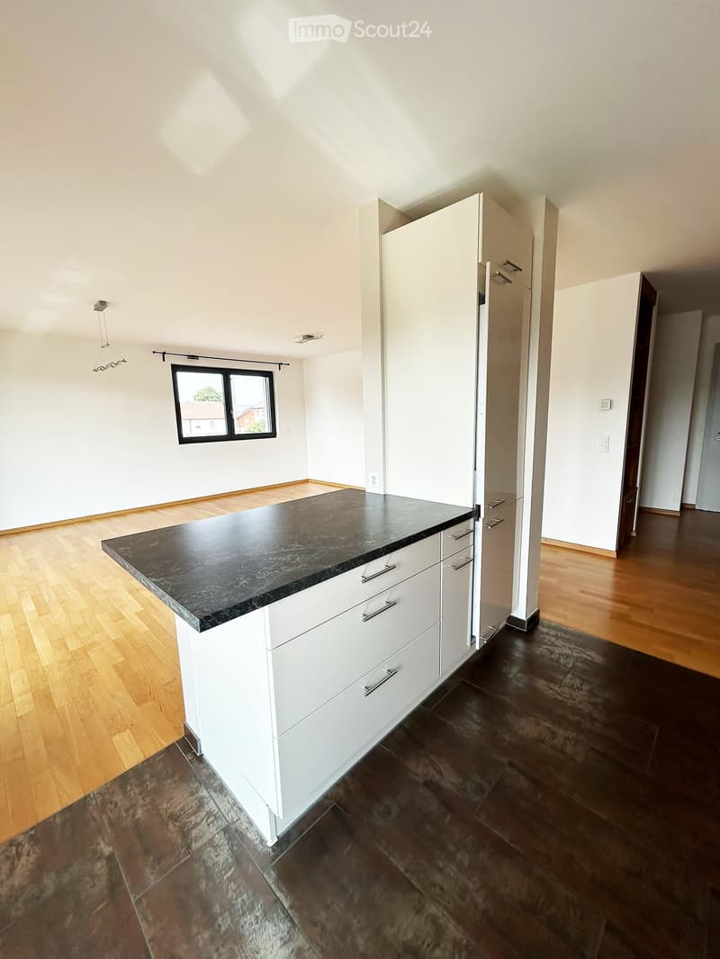 Modern kitchen with white cabinets, a black granite countertop island, and a refrigerator. The floor is a mix of light wood and dark tiles.