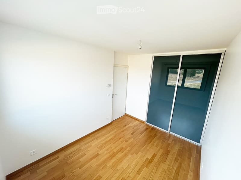 Empty room with light wooden flooring, white walls, and a sliding glass door leading to an outdoor area.