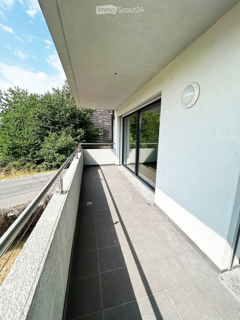 Modern balcony with tiled flooring, glass railing, and a view of greenery and a road.