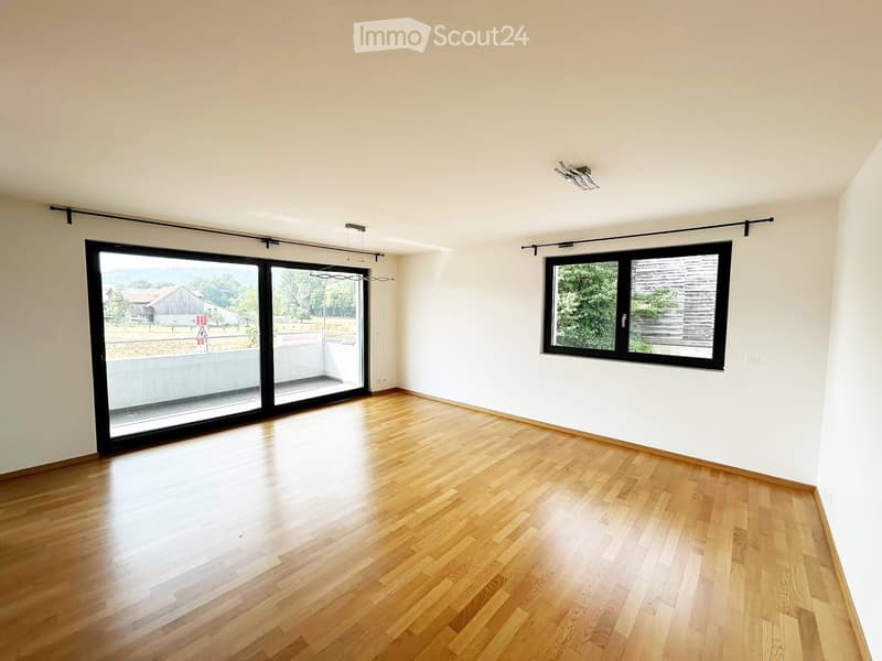 Empty room with wooden flooring, large sliding glass door, and a window with black frame. No furniture or equipment present.