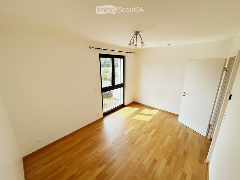 Empty room with wooden flooring, white walls, and a large glass door leading outside. No furniture or equipment is present.