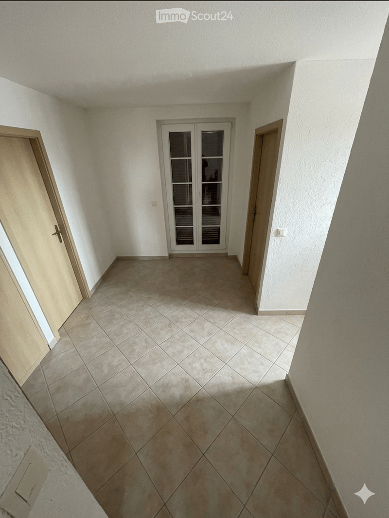 Empty hallway with tiled floor, white walls, and two doors, one with glass panels.