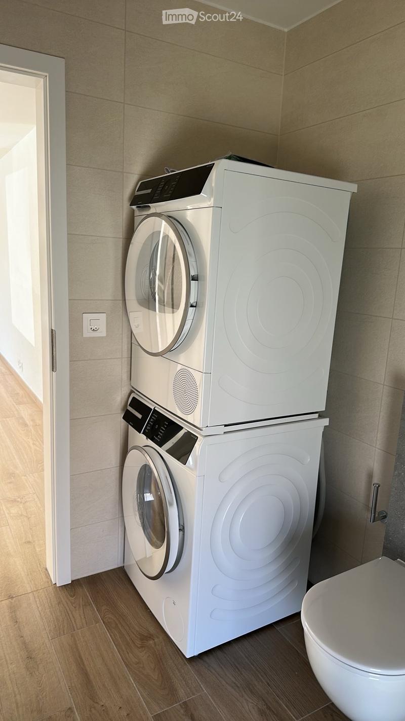 Bathroom with a washing machine and dryer stacked vertically, a toilet, and wooden flooring.
