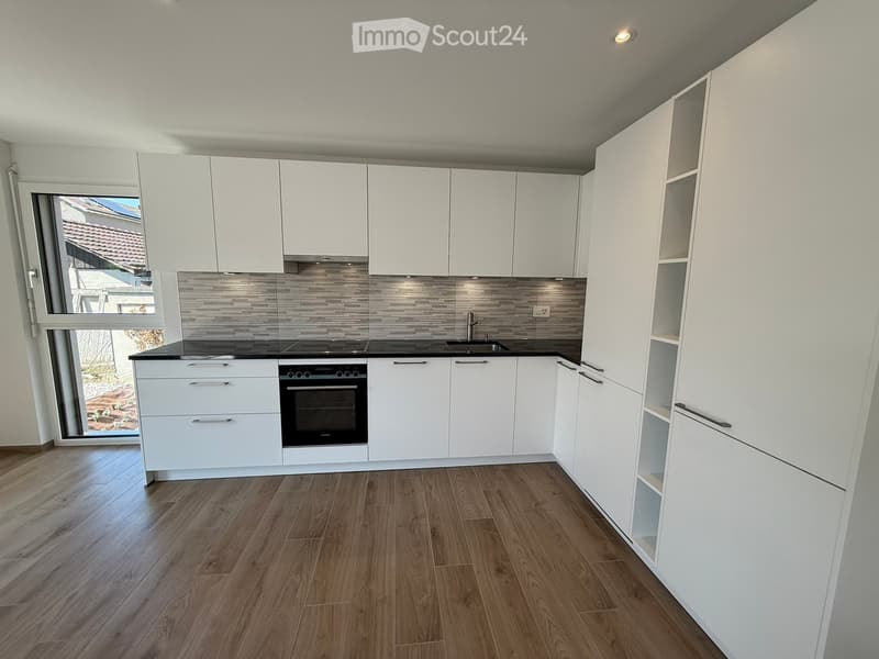 Modern kitchen with white cabinets, wooden flooring, and stainless steel appliances including an oven and sink.
