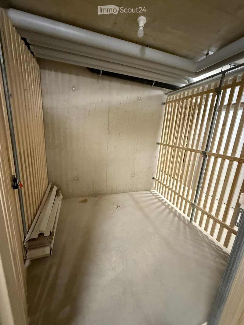 Empty hallway with unfinished walls, a wooden railing on one side, and a stack of wooden panels on the left. Natural light filters in from a window at the end.