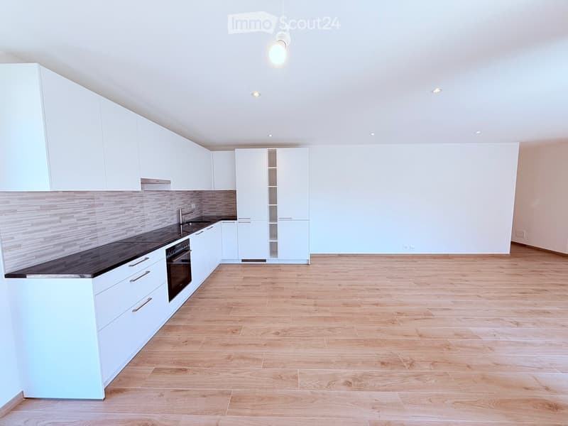 Modern kitchen with white cabinets, wooden flooring, and a black countertop. Features an oven, sink, and faucet.