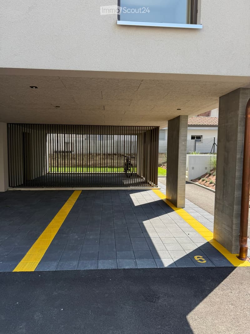 Modern building entrance with a covered driveway, black and yellow tiled floor, metal gate, and concrete columns.