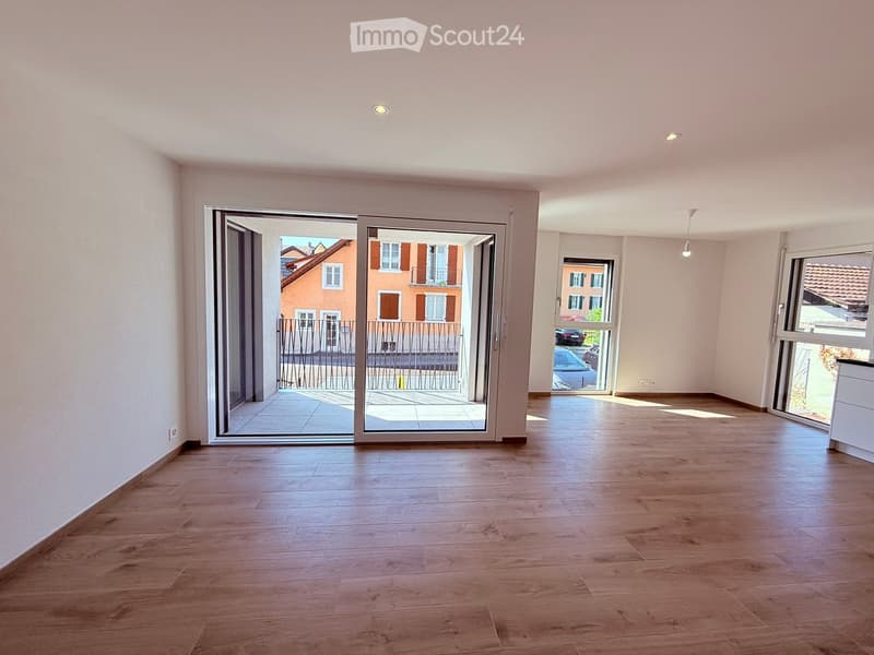 Empty room with wooden flooring, large sliding glass doors leading to a balcony, and natural light from windows.